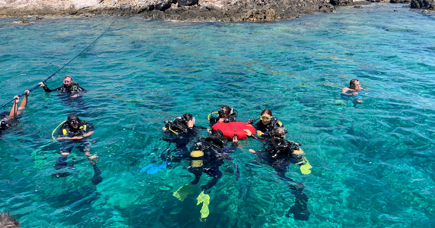 Duikers in turkoois water bij een rotsachtige kust voor training.